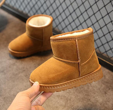 Brown snow boots with fur lining held by a hand on a neutral background